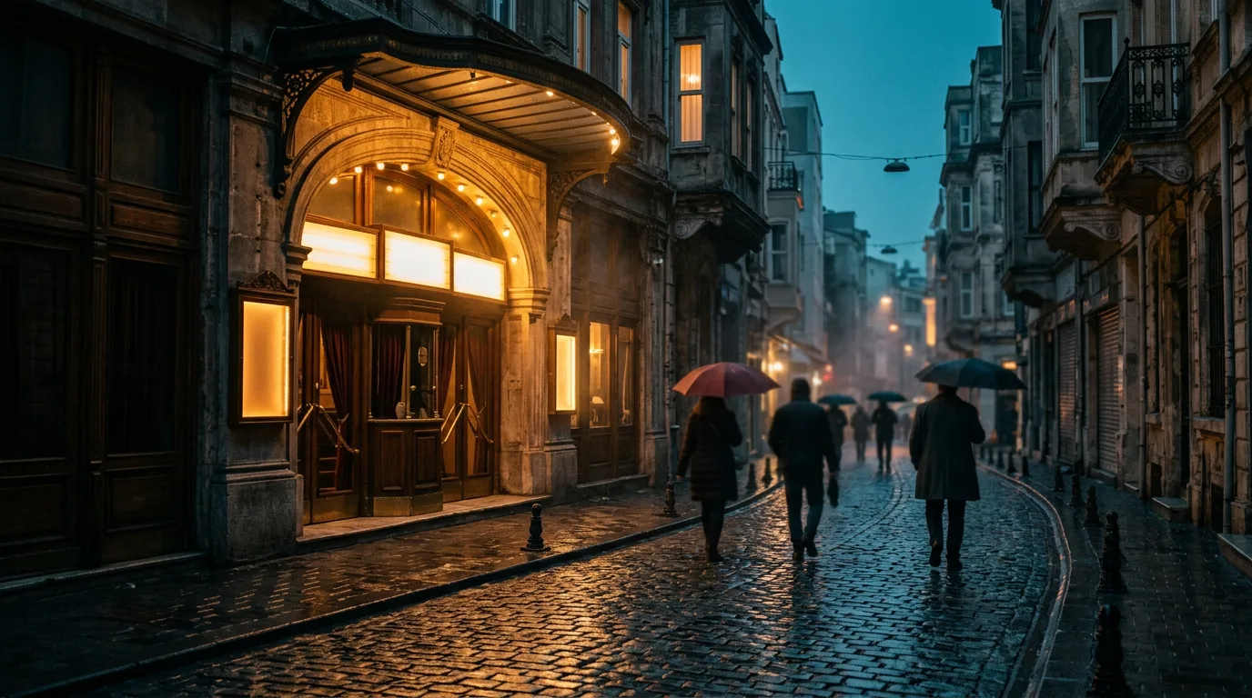 Beyoğlu'nda yağmurlu bir akşam, ıslak kaldırımda eski bir sinema girişinin sıcak ışığı ve silüet halinde yayalar.